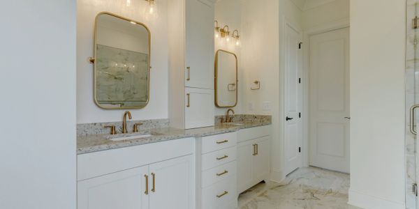 Modern bathroom with dual sinks, gold fixtures, and marble flooring.