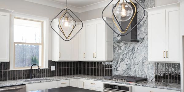 Modern kitchen with white cabinets, granite countertops, and geometric pendant lights.