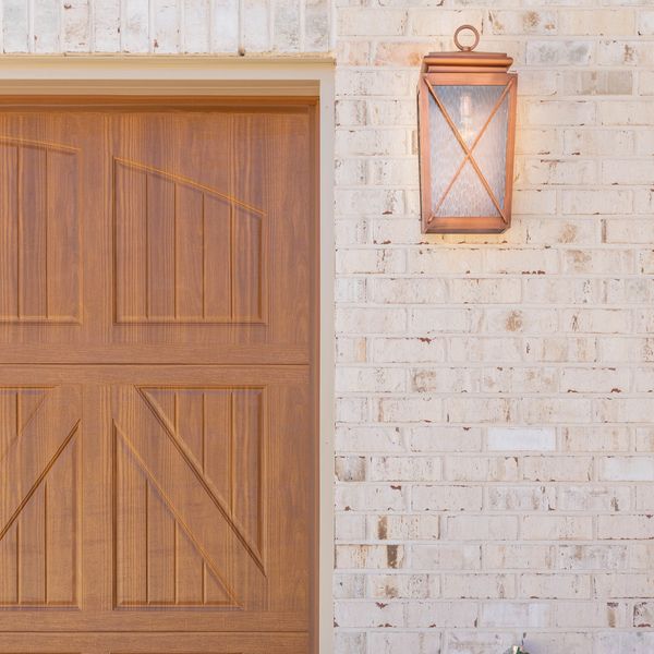 Wooden garage door beside a wall-mounted lantern on a white brick wall.