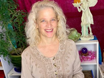 Smiling woman with curly hair in a beige embroidered top indoors.