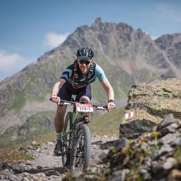Mountain biker riding on a rocky trail with a mountain backdrop.