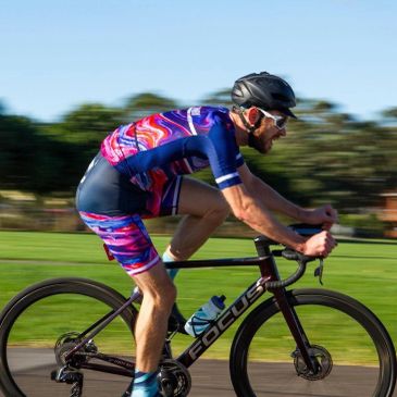 A cyclist in colorful gear rides a Focus bike on a sunny day.