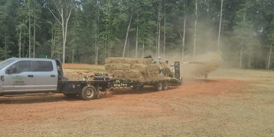 A truck towing a flatbed trailer carrying a tank covered in camouflage netting.