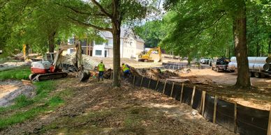 Construction workers installing erosion control fencing near trees on a soil slope.