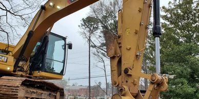 A yellow CAT excavator at a construction site near trees and buildings.