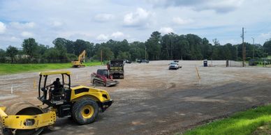 Construction vehicles prepare a large cleared area, possibly for paving or development.