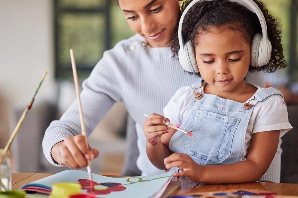 A child painting with a trusted adult during art class