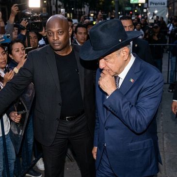 Man in a blue suit and black hat with a security guard.