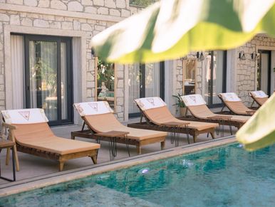 Poolside lounge chairs with towels at a stone building in sunlight.