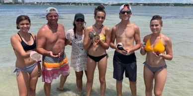 Group of six people posing in shallow water at the beach on a sunny day.