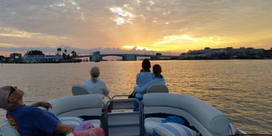 People relaxing on a boat at sunset near a marina and bridge.
