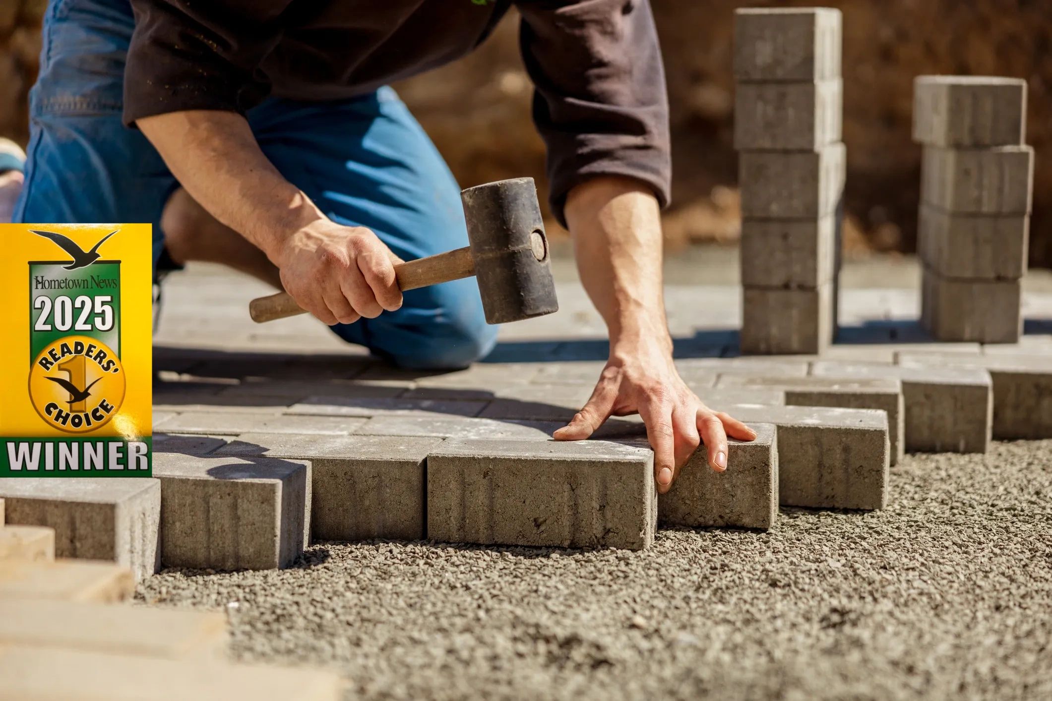 Worker laying concrete blocks with a mallet on gravel base.
