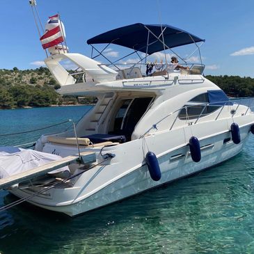 A white yacht docked in clear blue water with a person relaxing on the upper deck.