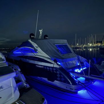 Luxury yacht illuminated with blue lights docked at a marina at night.