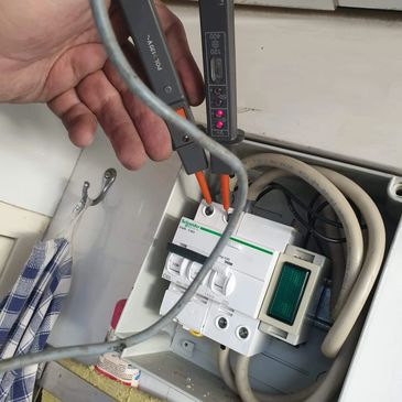 Hand using a voltage tester on an electrical circuit breaker panel.