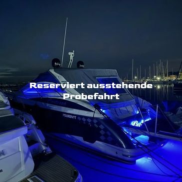 Luxury yacht illuminated with blue lights docked at a marina at night.