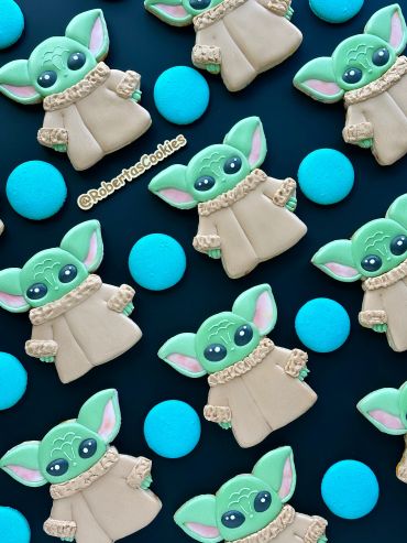 Cookies shaped like Baby Yoda with blue round cookies on a black background.