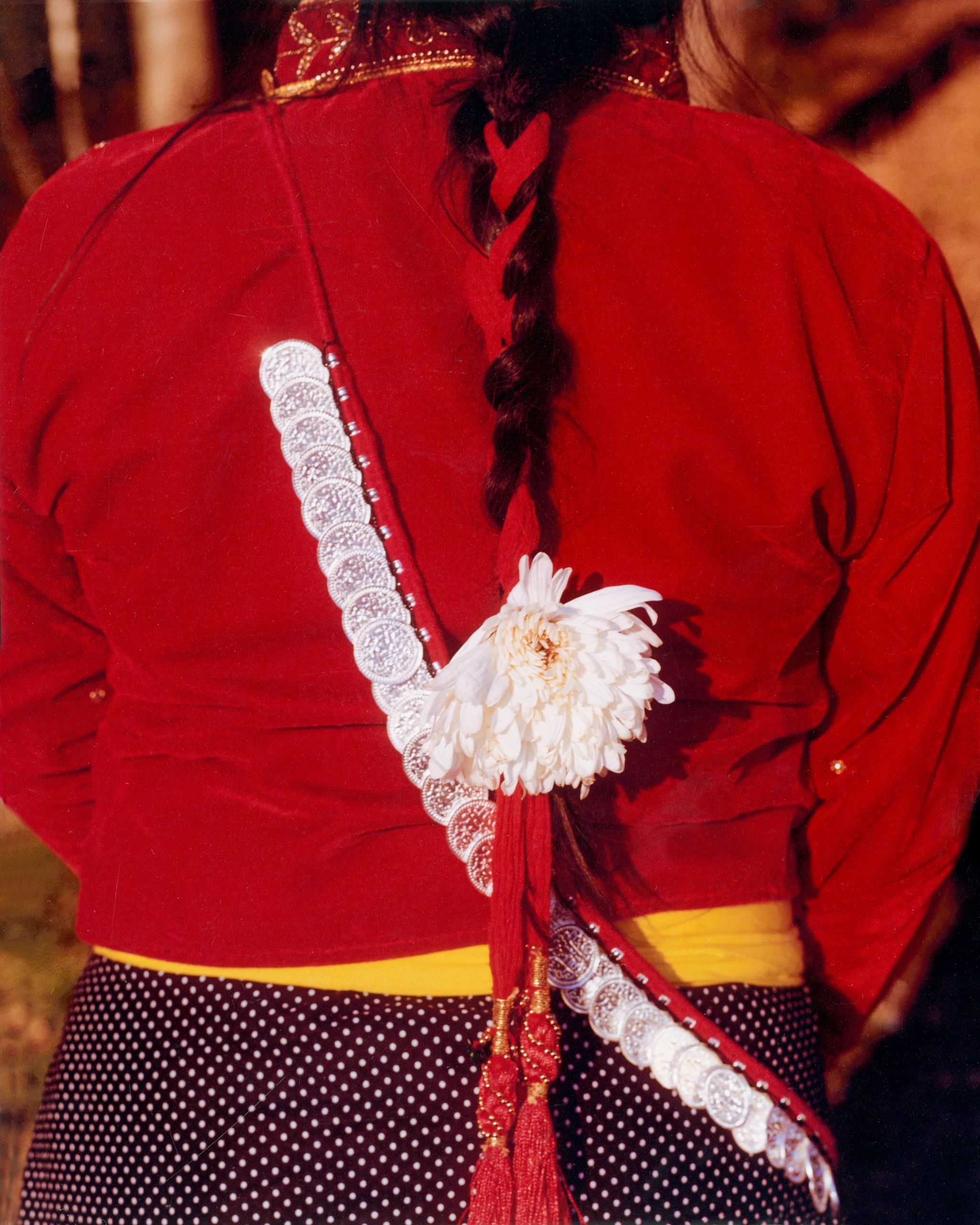 Person in traditional attire with braided hair and white flower accessory.