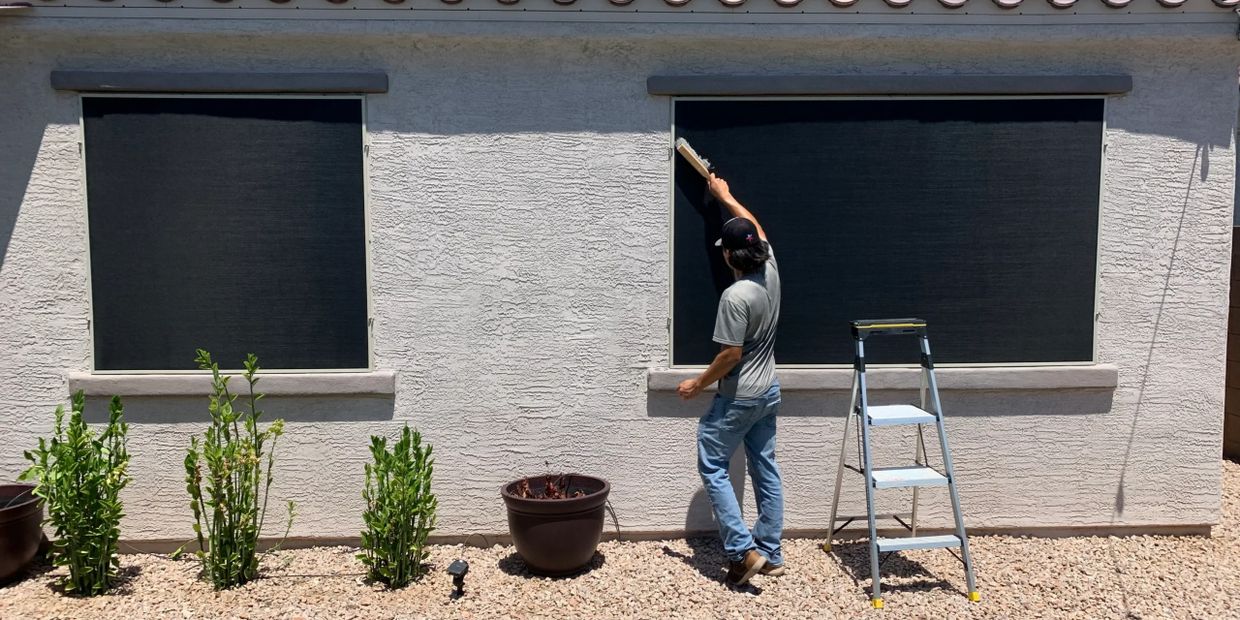 Man installing black window screens on a house exterior.