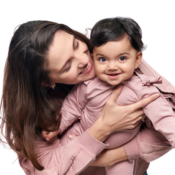 A joyful mother lovingly embraces her smiling baby dressed in pink.