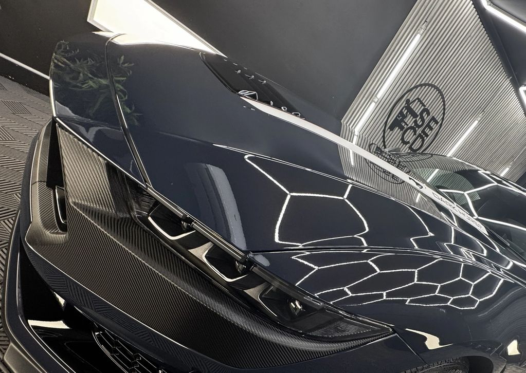 Close-up of a sleek black sports car with carbon fiber details under bright showroom lights.
