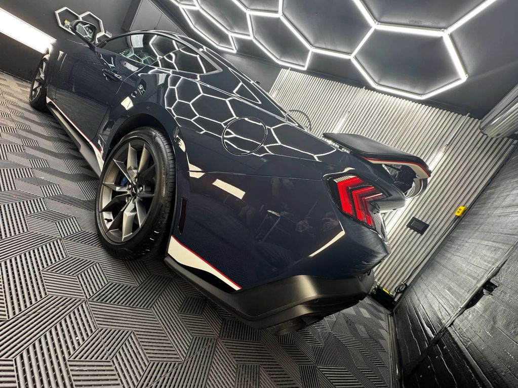 Sleek black sports car with glowing hexagonal ceiling lights in a modern garage.