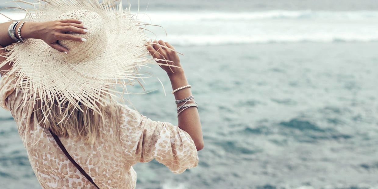 Woman in a straw hat gazing at the ocean waves.