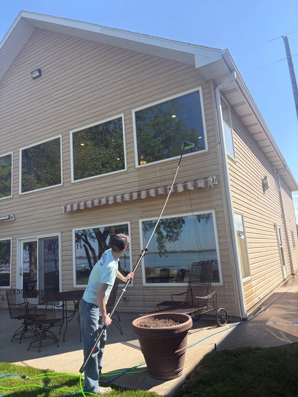 Man cleaning high windows of a beige house with an extended pole.