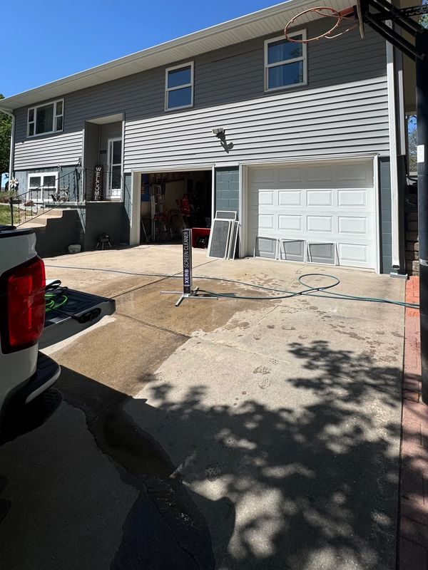 Driveway with cleaning equipment outside a two-story house with an open garage.