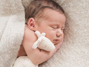 A sleeping baby wrapped in a cosy blanket and snuggling a teddy 