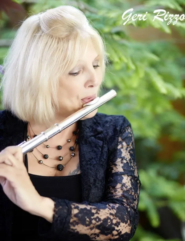 Blonde woman playing a silver flute in a natural setting.