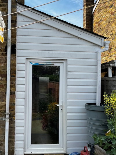 Small white garden shed with a glass door and water barrel beside it.