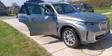 Silver BMW SUV parked with open doors on a driveway under clear sky.