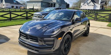 Black Porsche SUV parked on a driveway in a suburban neighborhood.