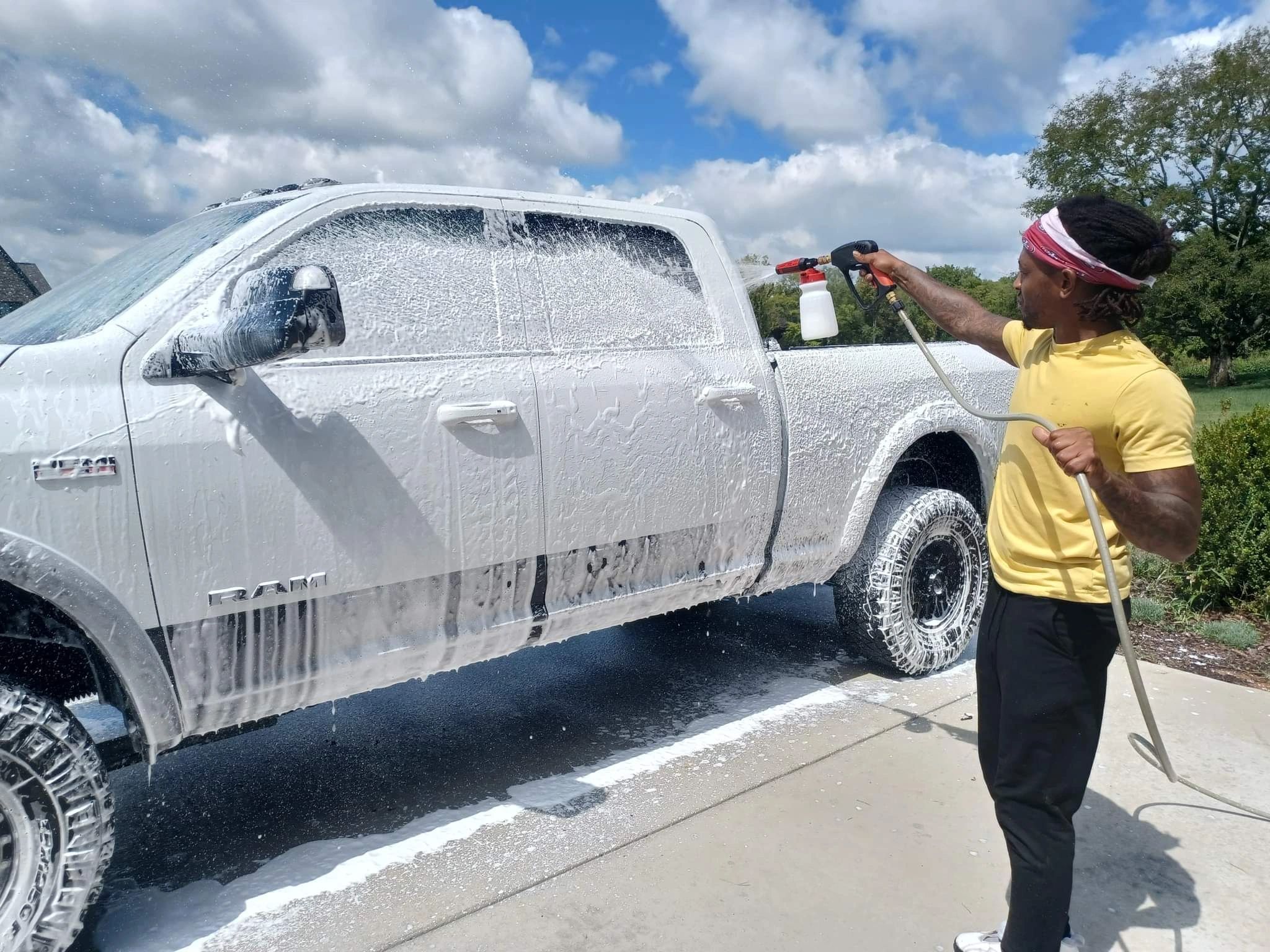 Man washing a white RAM truck with foam on a sunny day.