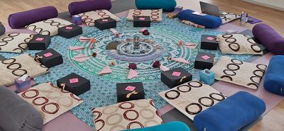 A circular arrangement of cushions and boxes on a patterned rug for a group activity.