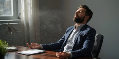 Man in suit meditates peacefully at his desk with eyes closed.