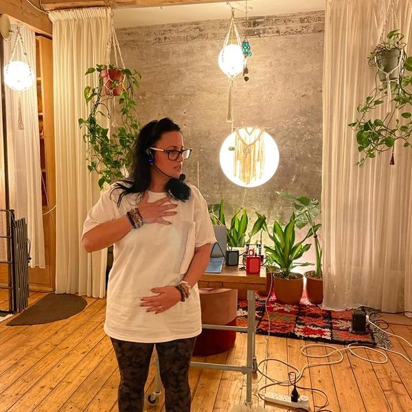 Woman in a cozy room with plants and warm lighting, wearing a white shirt and glasses.