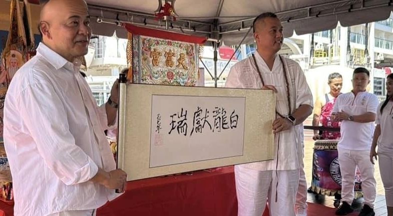 Two men holding a scroll with Chinese calligraphy at a cultural event.