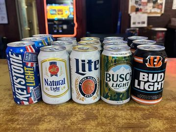 Assorted light beer cans lined up on a wooden surface in a bar setting.