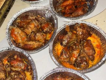 Five foil containers filled with cooked chicken wings in sauce.