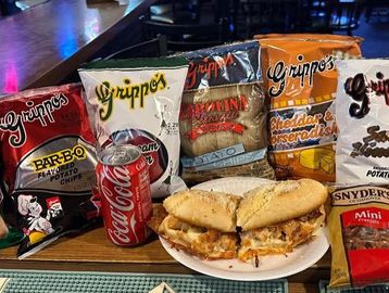 A sandwich with various chip bags and a can of Coca-Cola on a table.
