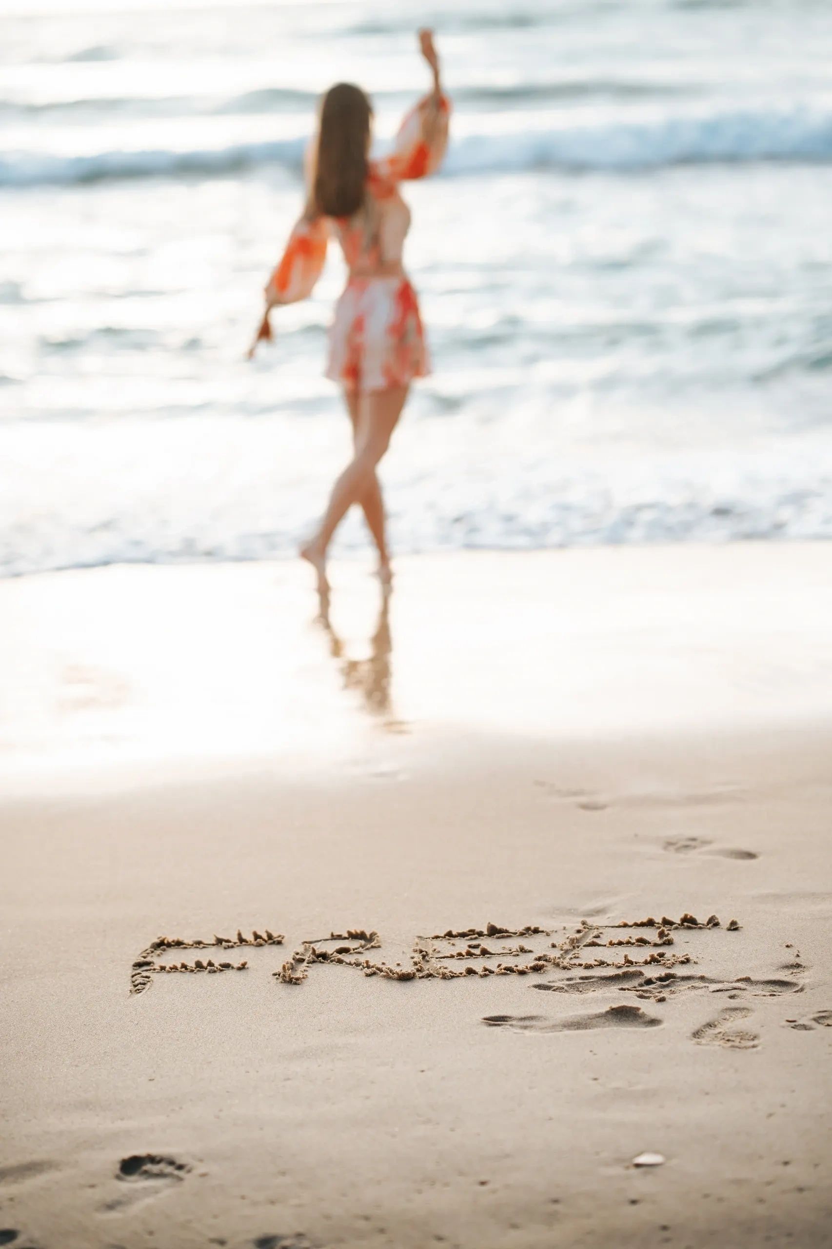 the word "free" written in the sand with a woman in the background, walking towards the ocean