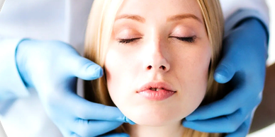 Hands wearing blue medical gloves, feeling the neck and jawline of patient with closed eyes