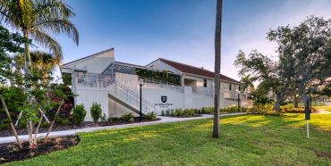 Modern white building with greenery and palm trees under a clear sky.