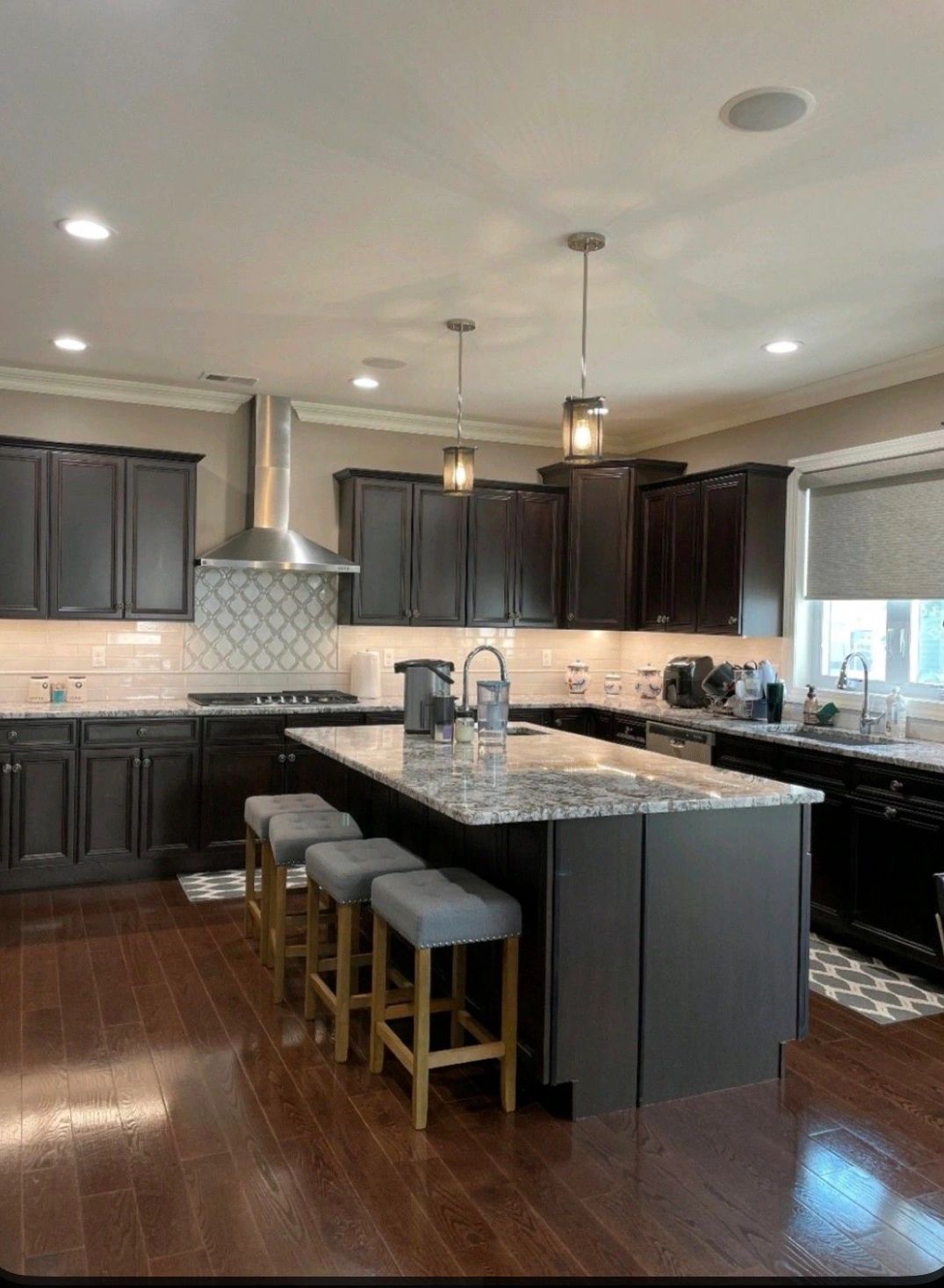 Modern kitchen with dark cabinets, granite island, and wooden stools.
