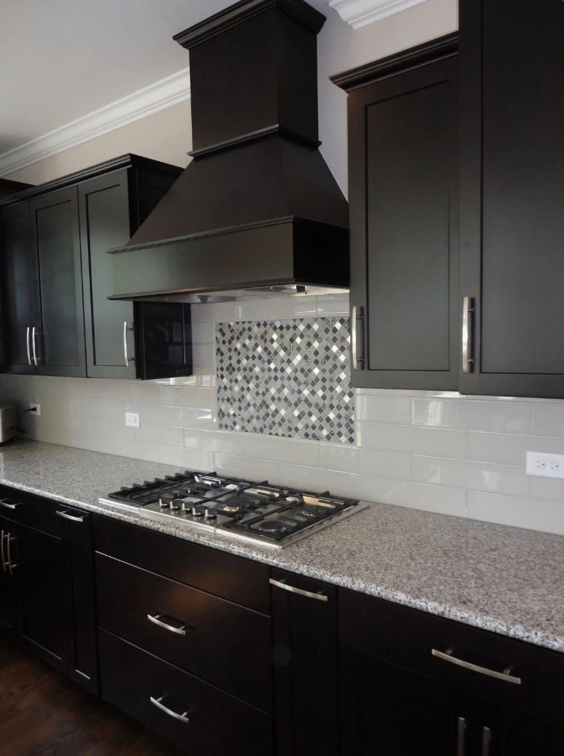 Modern kitchen with dark cabinets, granite countertop, and mosaic tile backsplash.
