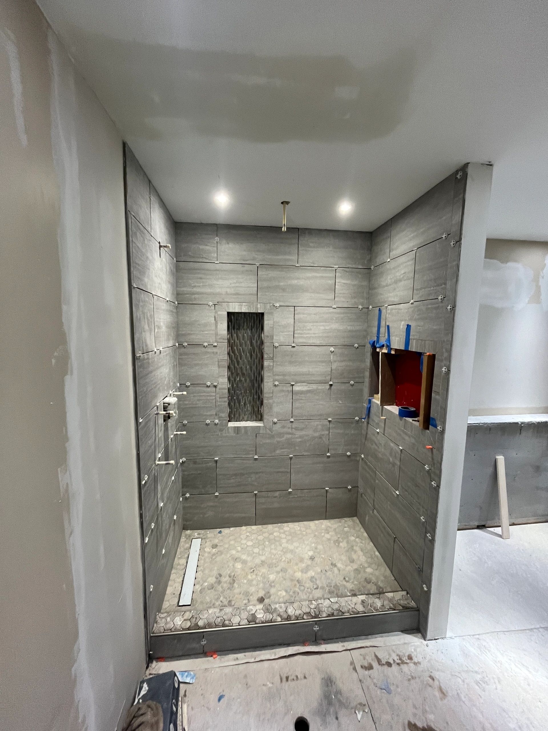 Shower under construction with gray wall tiles and pebble floor.