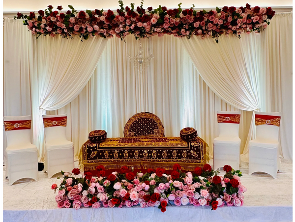 The wedding stage is elegantly decorated with flowing white drapes and lush floral roses. 