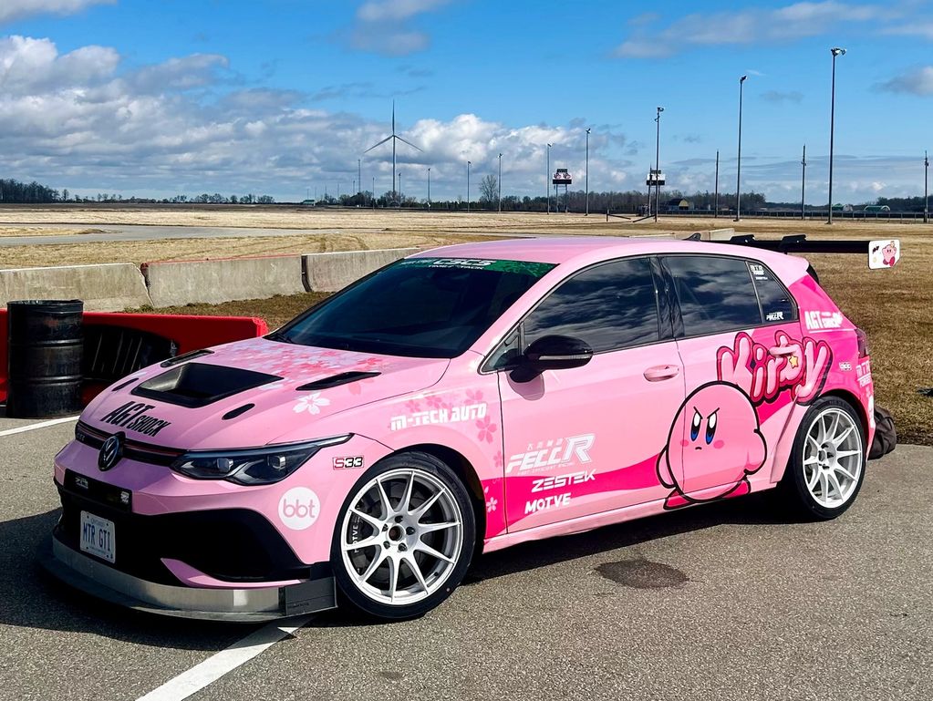 Pink Volkswagen car with Kirby theme and racing decals parked on a track.